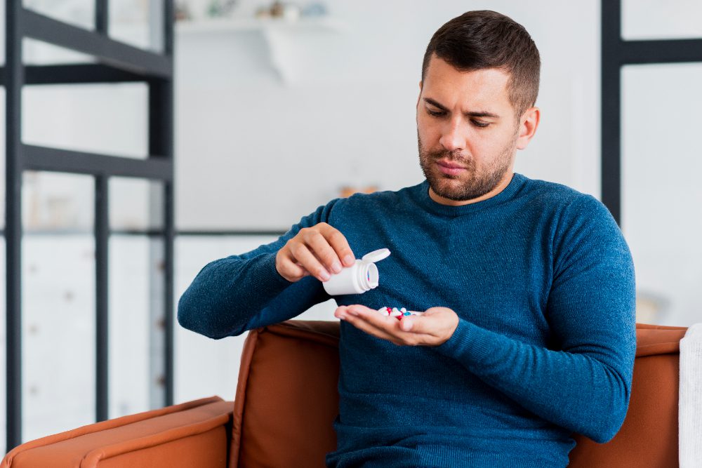 Person in blue sweater pouring pills into hand from a bottle